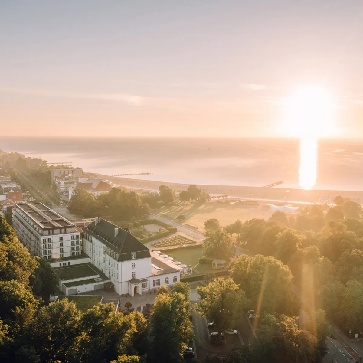 Eine Stadt mit Bäumen und einem Gewässer bei Sonnenaufgang.