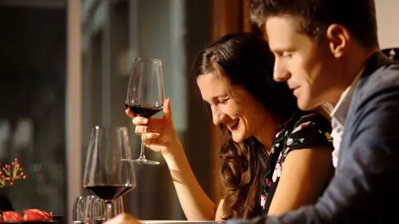 Eine Frau und ein Mann sitzen nebeneinander und trinken ein Glas Rotwein.