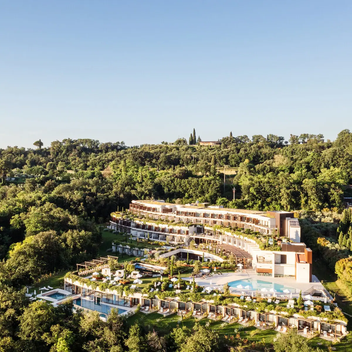 Das Gebäude des A-ROSA Gardasee aus der Luft aufgenommen. Man erkennt die treppenförmige Bauweise und den weitläufigen Garten Außerdem sieht man die Pools auf den verschiedenen Ebenen.