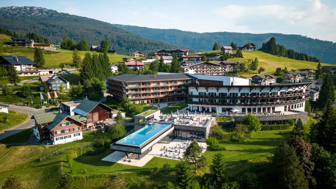 Gebäude mit einem Infinity-Pool inmitten eines Bergdorfes, umgeben von Bäumen und einer Landschaft mit Bergen.