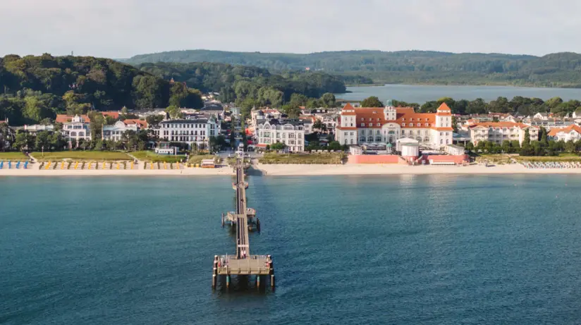 The Kurhaus Binz can be seen from the sea. In front of it is the beach and a long jetty leads into the Baltic Sea. 