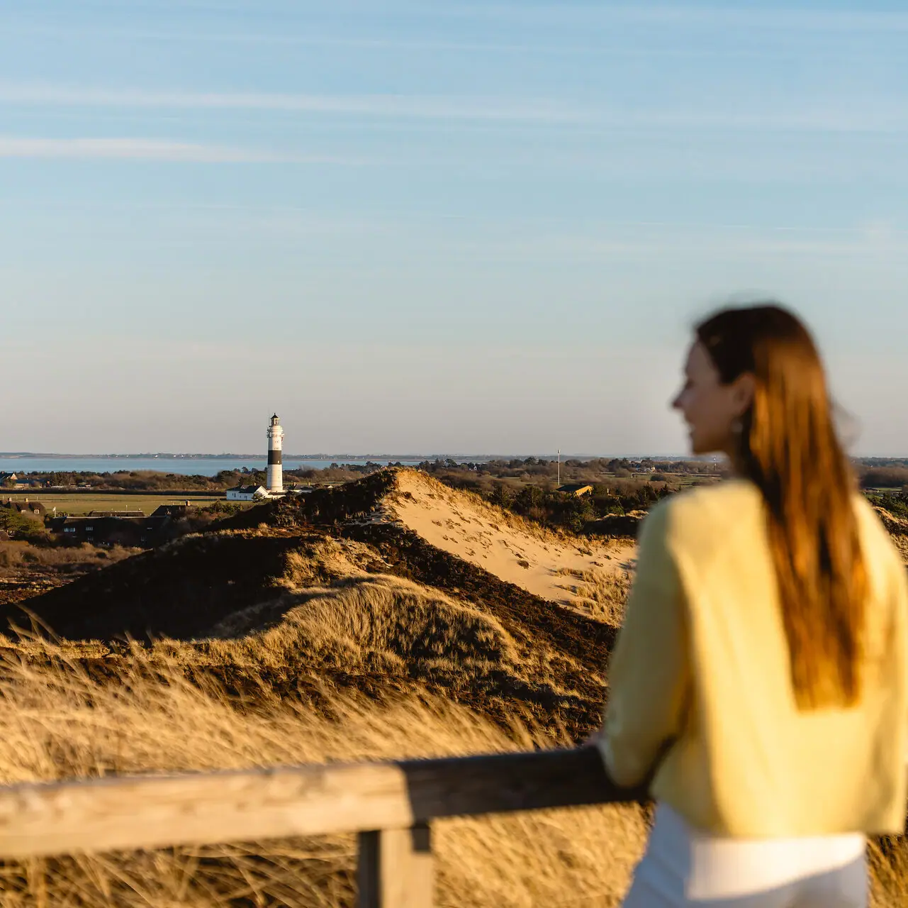 Eine Frau steht auf einem Zaun und blickt auf einen Leuchtturm auf Sylt.