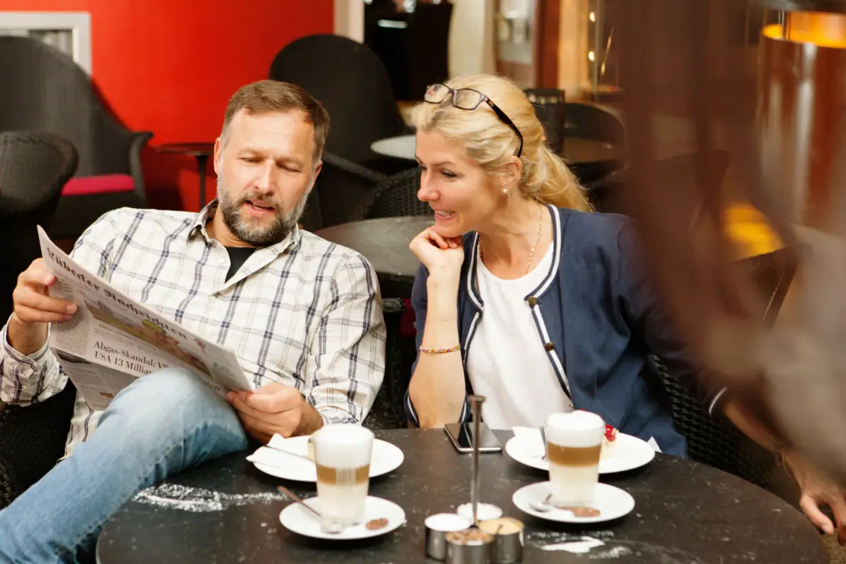 Ein Mann und eine Frau sitzen an einem Tisch mit Kaffee und einer Zeitung.