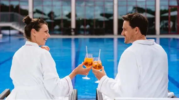 Ein Mann und eine Frau in Bademänteln halten Getränke am Pool.