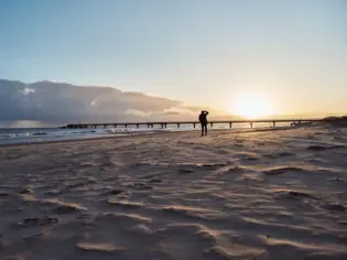 Person steht am Strand bei Sonnenuntergang.