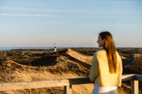 Uwe Düne Sylt Eine Frau steht auf der Uwe Düne Sylt und blickt auf einen Leuchtturm.