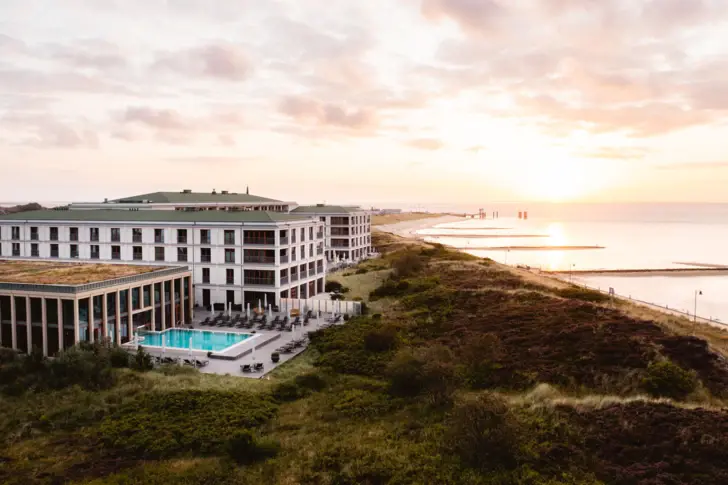 Das A-ROSA Sylt mit Pool umgeben von Dünen und mit Blick auf die Nordsee.