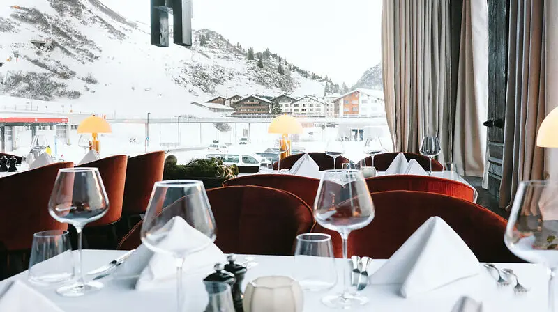 Elegant gedeckter Tisch mit Geschirr und Weingläsern, mit Blick auf verschneite Berge.