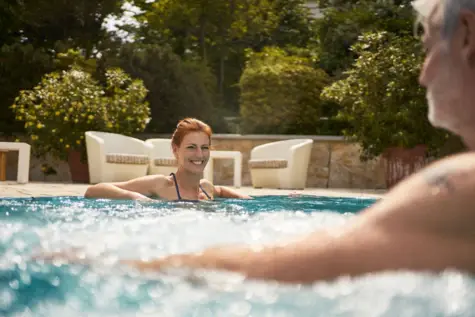 Ein Paar schwimmt glücklich in einem Außen-Whirlpool und lacht.