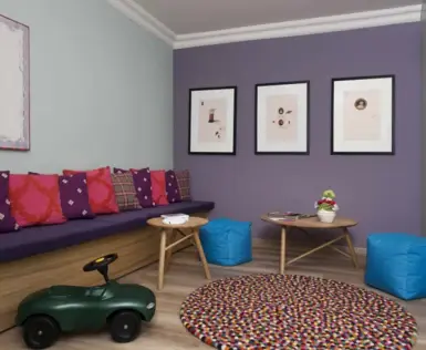 A small children's room with a long bench on the left wall, a green bobby car, a round carpet and two small tables and beanbags.