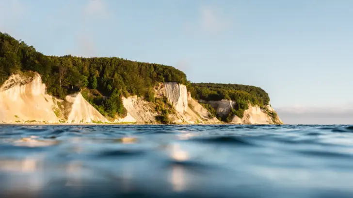 Blick auf eine Wasserfläche mit einer Klippe und Bäumen.