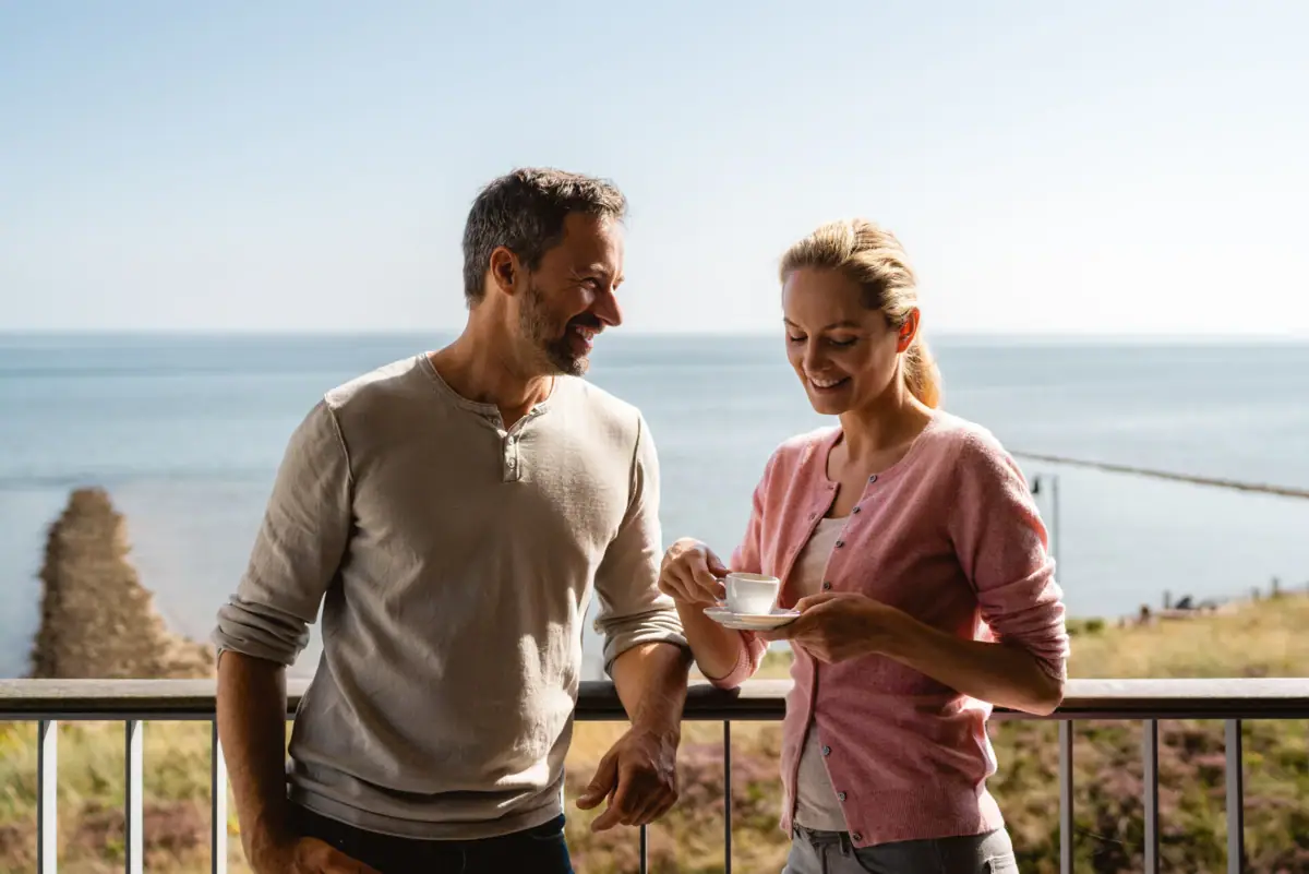 Ein Mann und eine Frau stehen auf einem Balkon mit Blick aufs Meer.