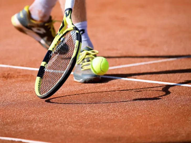 Eine Ansicht des Tennisfelds von Männerbeinen und einem Tennisschläger mit Ball. 