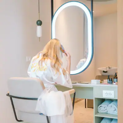 Eine Frau im Bademantel kämmt sich die Haare vor einem Spiegel.