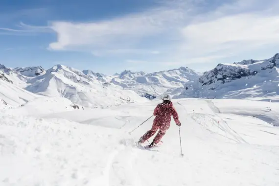 Person in lila Schneekleidung beim Skifahren auf verschneitem Berghang.