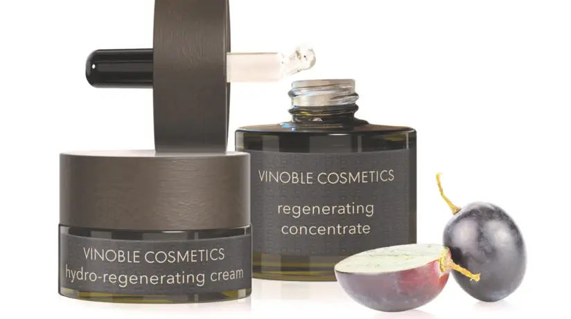 High-quality skincare products from VINOBLE COSMETICS, including a hydro-regenerating cream and a regenerating concentrate, presented alongside a halved bunch of grapes. The elegant packaging and natural grape reflect the concept of natural ingredients and luxurious skincare.