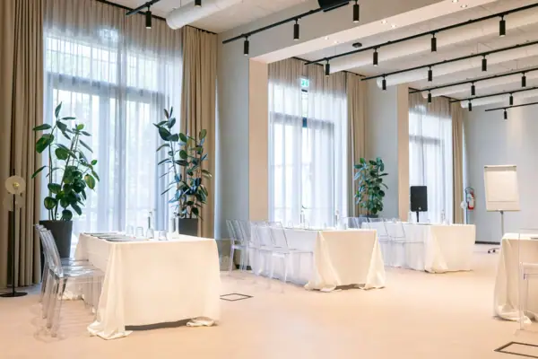 Heller Indoor-Eventraum mit gedeckten Tischen und großen Fenstern für Hochzeitsfeiern.