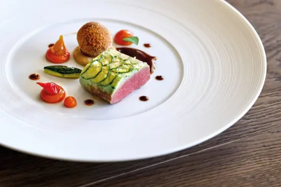 Ein Teller mit kunstvoll garniertem Essen auf einem Holztisch.