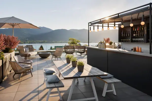 Die Terrasse vom A-ROSA Tegernsee mit einer Bar und Tischen sowie dem spektakulärem Blick auf den Tegernsee und die Berge.