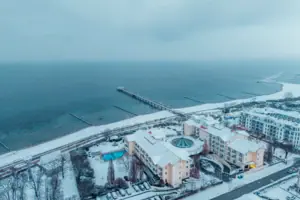 Schneebedeckter Strand mit Gebäuden und einem Pier im Winter.