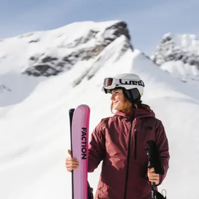 Frau mit Skiern und Stöcken vor schneebedeckten Bergen