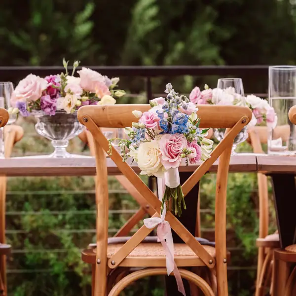 Holzstühle einer Hochzeitstafel, mit kleinen Sträußen aus Rosen und Bändern festlich geschmückt.