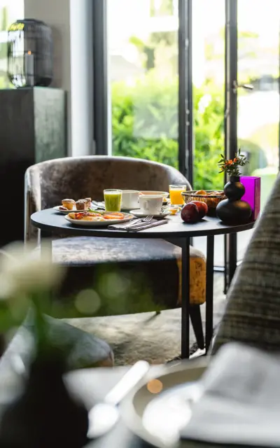 A table with food in an interior, near a window, decorated with a vase.