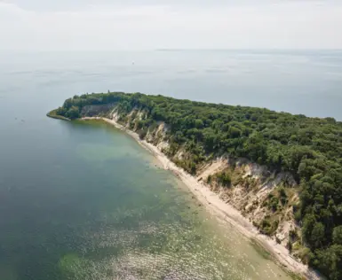 Luftaufnahme eines Strandes mit Bäumen, umgeben von klarem Wasser und Küstenlandschaft.