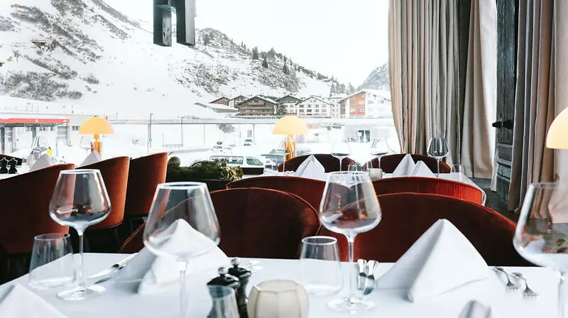 Elegantly set restaurant table with tableware and wine glasses, overlooking snowy mountains.