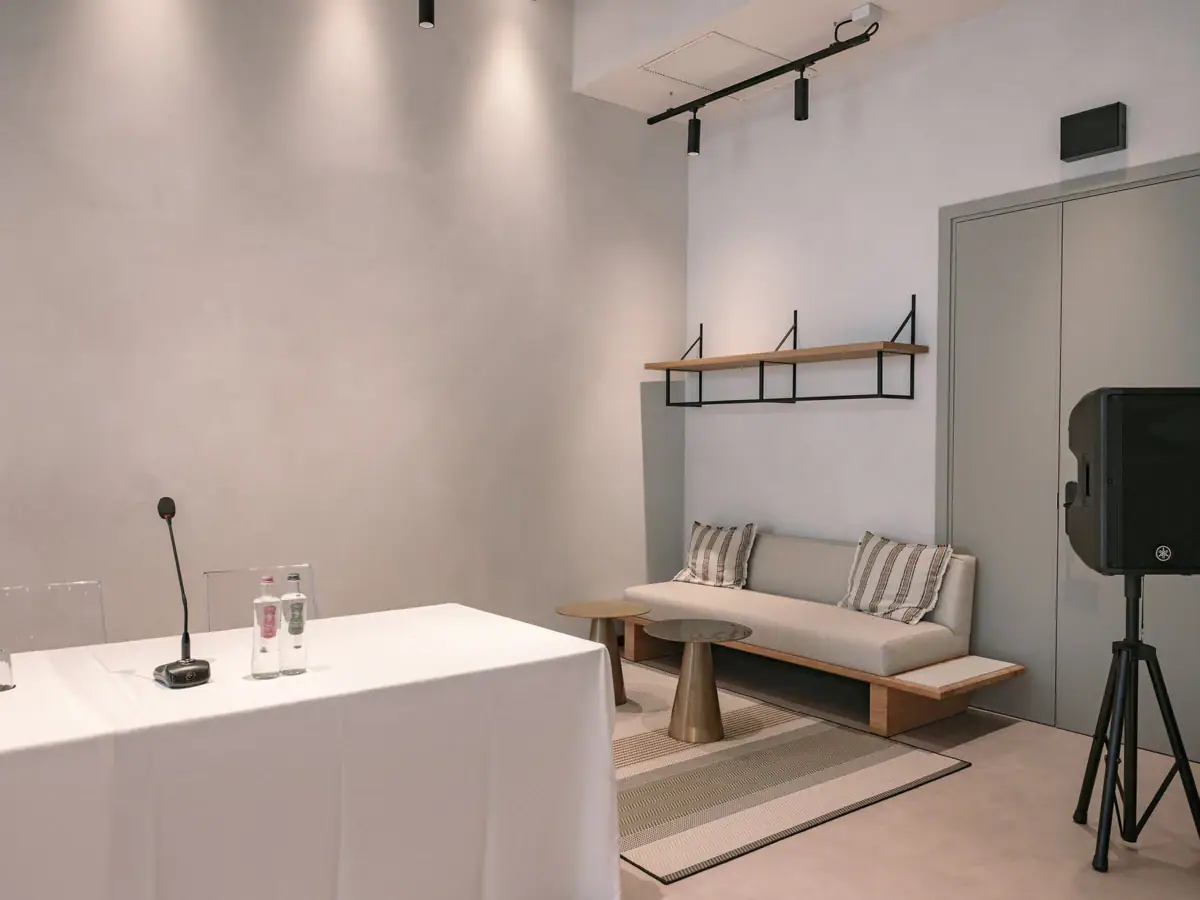 Ein Tagungsraum mit einem weißen Tisch und einer Couch. Auf dem Tisch steht ein Mikrofon, neben dem Tisch steht ein Lautsprecher.