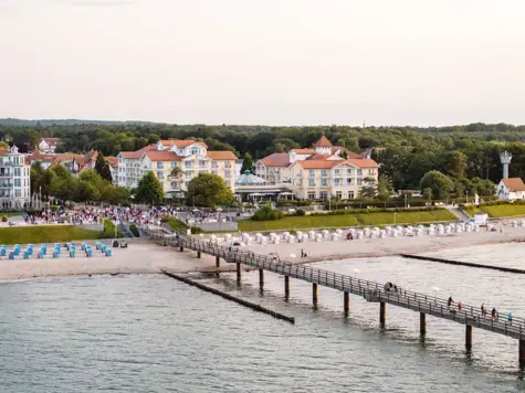 Luftansicht des A-ROSA Kühlungsborn direkt am Strand mit eine langen Steg davor, der auf das Wasser hinaus führt. 