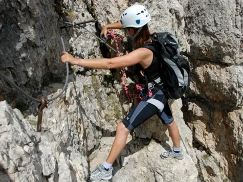 Frau klettert an einer Felswand, ausgestattet mit Klettergurt und Helm.