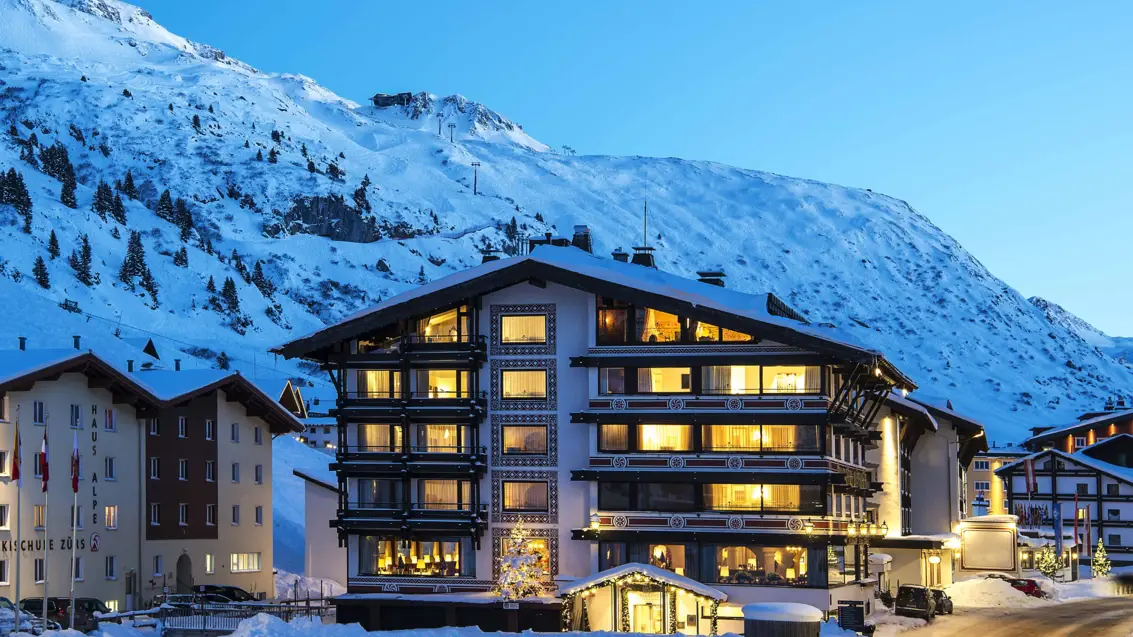 A multi-storey house at dusk stands in front of a snow-covered mountain.