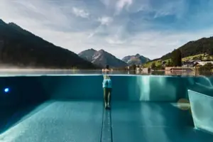 Eine Person steht in einem Pool mit Bergen im Hintergrund.