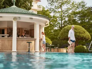 Eine Frau steht an einer Poolbar und ein Mann spaziert am Rand des Pools entlang.