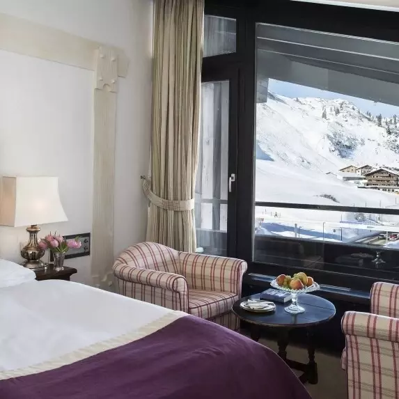 Einladendes Zimmer mit Bett, Stühlen und Tisch, mit Blick auf schneebedeckte Berge.