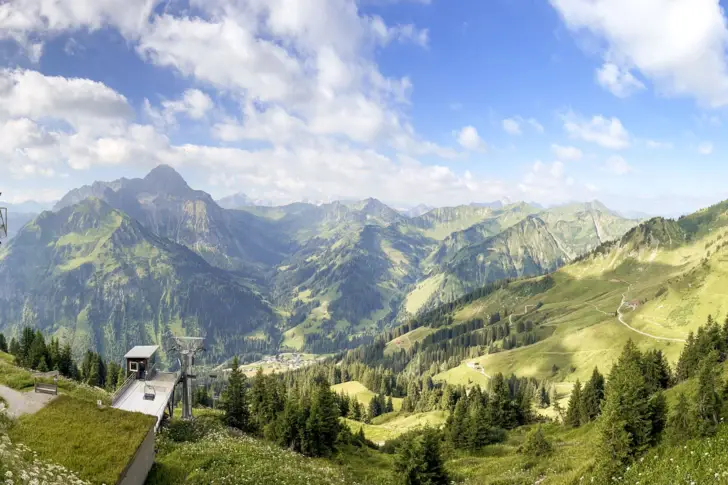 Berglandschaft mit Gebäude und Bäumen unter blauem Himmel mit einigen Wolken.