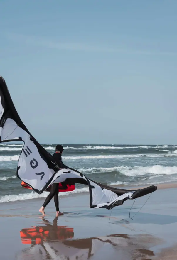 Ein Kitesurfer geht mit seinem Kite am Ufer der Ostsee lang.