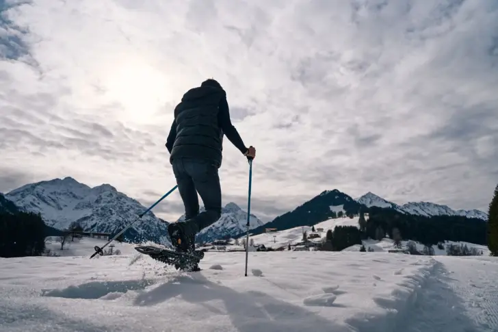 Person mit Schneeschuhen und Stöcken auf verschneiter Landschaft.