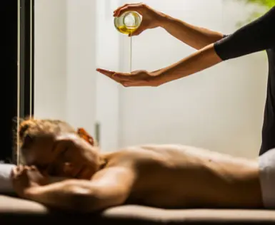 Person gießt Öl in ihre Hand bei einer Massage einer anderen Person.