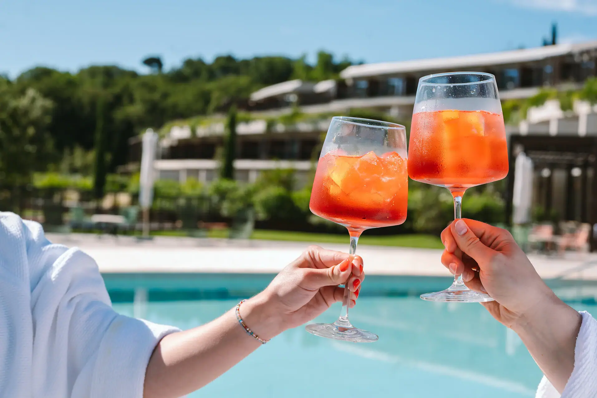 Hände halten zwei mit Aperol und Eis gefüllte Gläser.