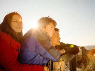 Eine Familie lehnt an einem Zaun, lächelt und trägt Winterkleidung.