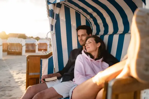 Ein Mann und eine Frau sitzen lächelnd auf in einem Strandkorb am Strand..