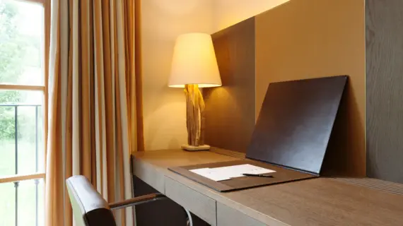 Ein Schreibtisch aus dunklem Holz mit einer Mappe, auf der ein Block und ein Stift liegt. In der hinteren Ecke ist eine Lampe zu sehen. 