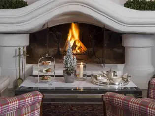 Two checkered armchairs stand in front of a coffee table and a fireplace with a fire burning in it.