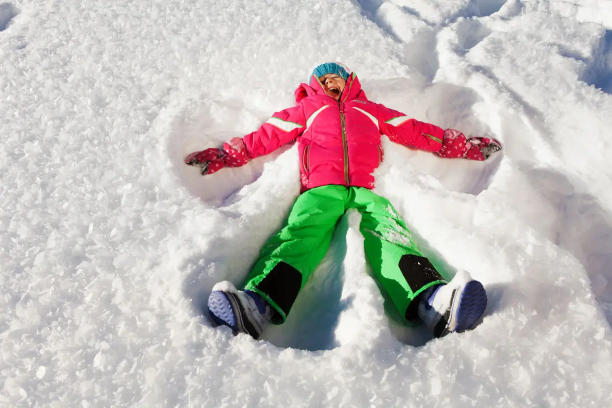 Ein Kind liegt im Schnee und macht einen Schneeengel.