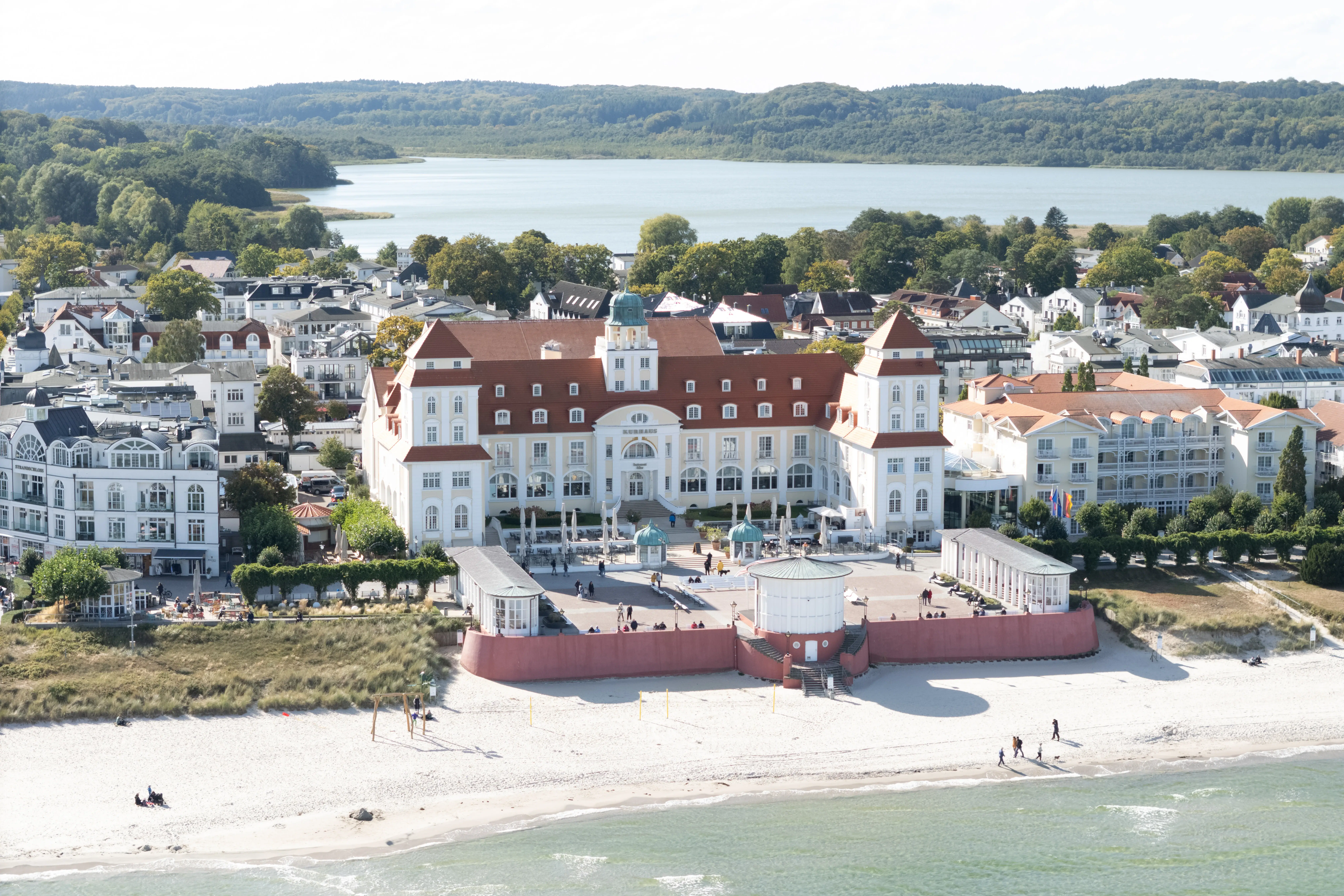 Großes weißes Gebäude im Stil der Bäderarchitektur an einem weißen Sandstrand mit dem Meer im Vordergrund.