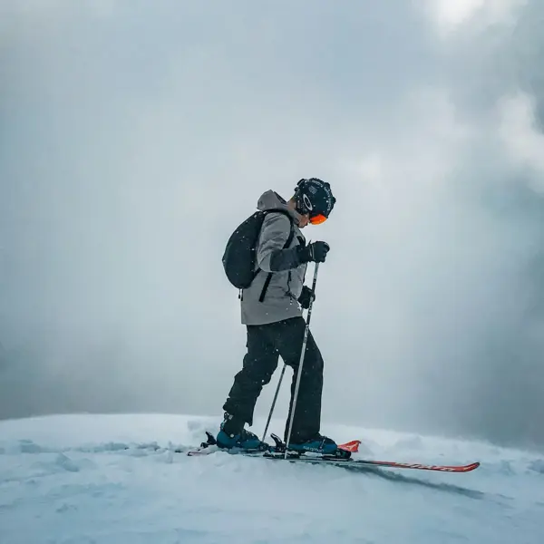 Ein Mann in Skiausrüstung steht auf Skiern und trägt einen Rucksack auf dem Rücken. 