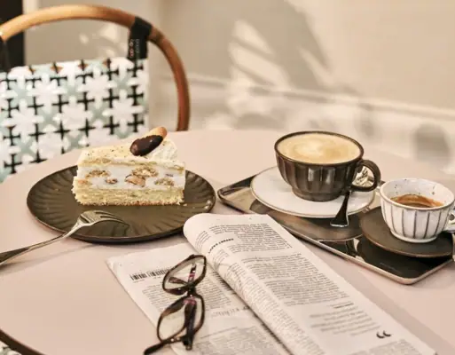 Ein Tisch mit einem Kaffeegedeck, einem Stück Kuchen und einer Zeitung