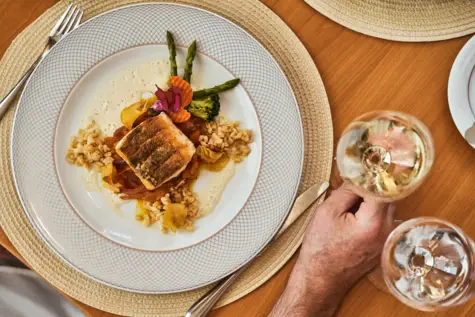 Ein Teller mit Essen und eine Hand, die ein Glas Wein hält.